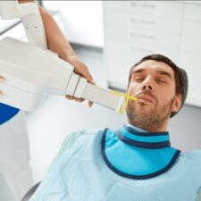 This image shows a photo of a man receiving an X-ray at a dental clinic