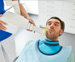 This image shows a photo of a man receiving an X-ray at a dental clinic